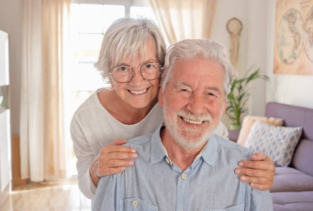 istock Smiling senior couple sitting at home hugging and looking at camera 1358543284