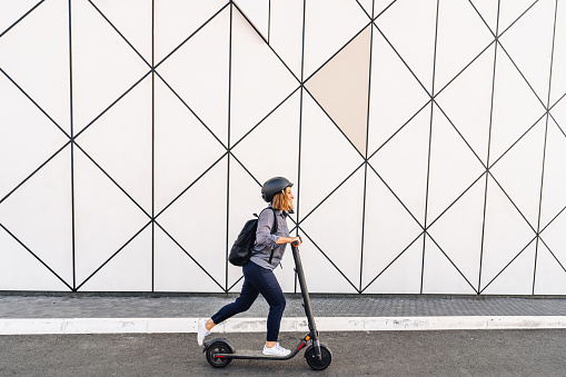 Photo of a mid adult woman riding an electric scooter, going to work