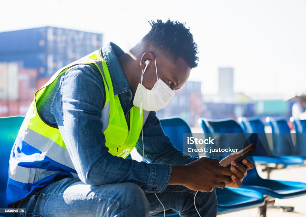 Relaxed African American worker man listening music podcast, Man wearing with disposable face mask sit at desk at container cargo site Music Stock Photo