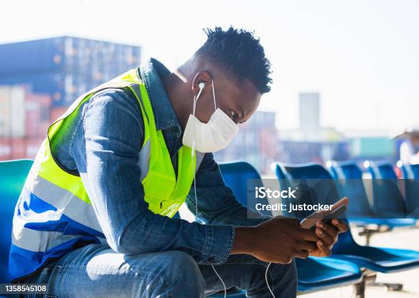 Relaxed African American Worker Man Listening Music Podcast Man Wearing With Disposable Face Mask Sit At Desk At Container Cargo Site Stock Photo - Download Image Now