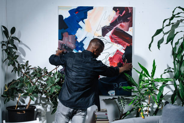 African american painter hanging his abstract colorful piece on the wall. stock photo