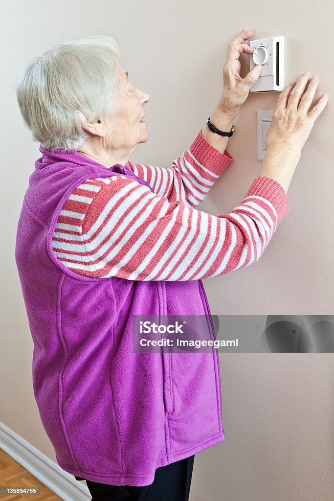 Mujer mayor ajustar su termostato - Foto de stock de Termostato libre de derechos