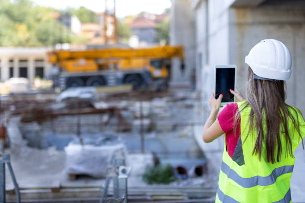 istock Young Female Building Worker is Standing at a Construction Site and Communicate with Coworkers or Friends Using a Smart Phone. 1358548894