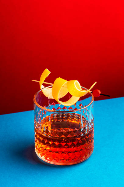 istock Sazerac, classic alcoholic cocktail with cognac, bourbon, absinthe, bitters, sugar and lemon zest. Dazzling red blue background with hard light and harsh shadows 1358553193