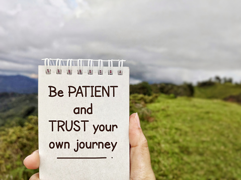 Be patient and trust your own journey. Text written on notepad background. Stock photo.