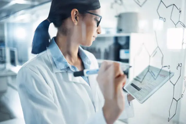 Photo of Shot of a young scientist solving equations on a glass screen in a laboratory