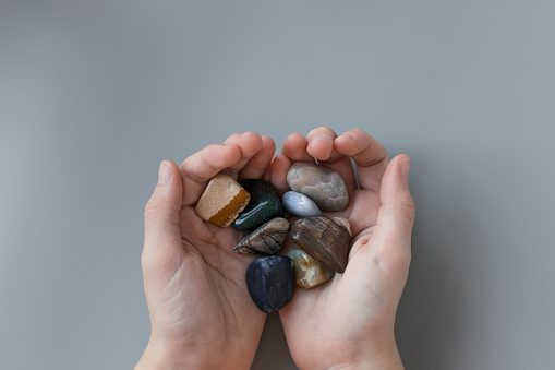 child holding various semiprecious stones in hands on gray background. Mineral stones collection, geology concept. top view, copy space