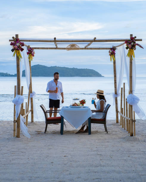 Romantic dinner on the beach in Phuket Thailand, couple man and woman mid age Asian woman and European man having a dinner on the beach in Thailand during sunset Romantic dinner on the beach in Phuket Thailand, couple man and woman mid age Asian woman and European man having dinner on the beach in Thailand during sunset. phuket beach party stock pictures, royalty-free photos & images
