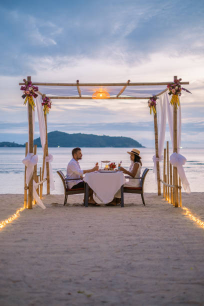 cena romantica sulla spiaggia di phuket thailandia, coppia uomo e donna di mezza età donna asiatica e uomo europeo che cenano sulla spiaggia in thailandia durante il tramonto - romance honeymoon couple vacations foto e immagini stock