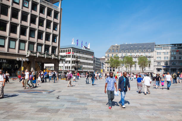 Pedestrians on square Domkloster in Cologne in summertime, People are waling in any direction. There are white people, immigrants, tourists and black people