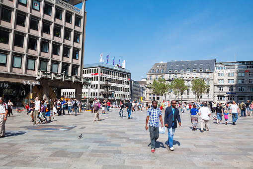 Pedestrians on square Domkloster in Cologne in summertime, People are waling in any direction. There are white people, immigrants, tourists and black people