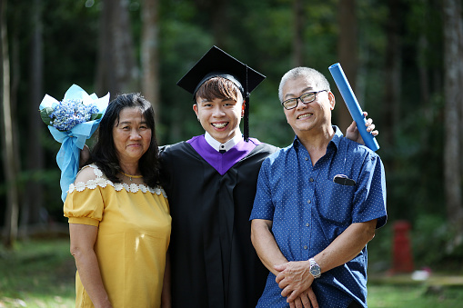 Portrait of an Asian young man in graduation gown together with his uncle and auntie.