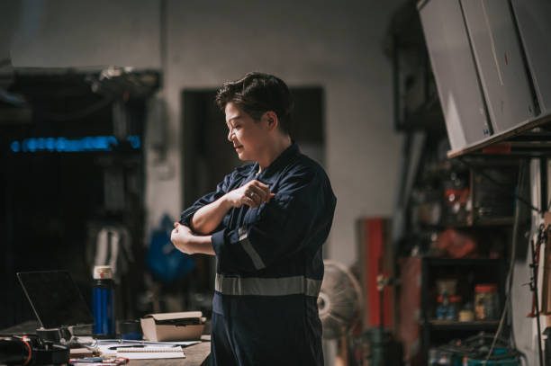 Asian Chinese Female Workshop Owner rolling sleeve getting ready to work at workbench Asian Chinese Female Workshop Owner rolling sleeve getting ready to work at workbench rolled up sleeves stock pictures, royalty-free photos & images