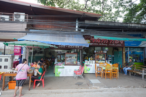 Some thai people are having breakfast at small restaurants at Sukothai heritage city in morning. Vendor woman is standing in bottom left of capture, There are several shops for food and beverage
