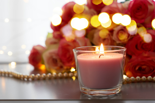 Burning candles with rose fresh flowers bouquet on gray table, close up home interior details with bokeh lights