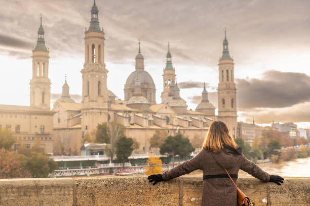 A young woman at sunset on the Stone Bridge next to the Basilica De Nuestra Señora del Pilar on the Ebro river in the city of Zaragoza, Aragon. Spain stock photo