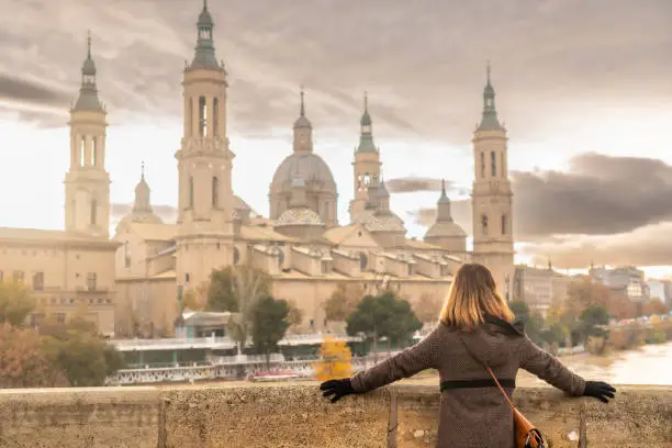 A young woman at sunset on the Stone Bridge next to the Basilica De Nuestra Señora del Pilar on the Ebro river in the city of Zaragoza, Aragon. Spain