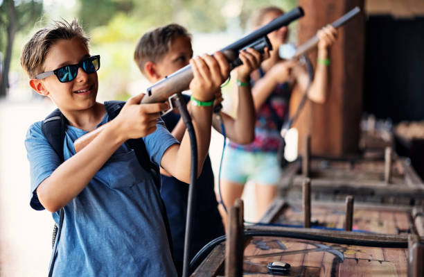 Three kids having fun playing target shooting game at funfair. Kids are using laser toy weapons to shoot targets.\nCanon R5