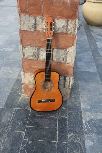 istock Classical brown guitar placed Infront of Brown Bricks- classical guitar against a brick wall-wall and floor background Vertical Orientation 1358591993