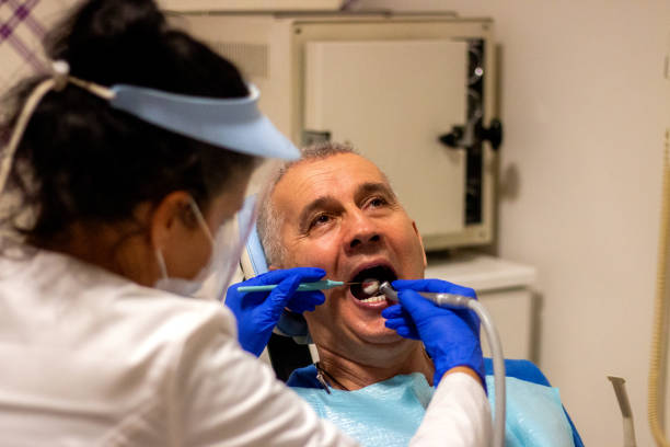 istock Middle-aged man is sitting on dentist chair while dentist is working on his ill tooth. 1358595929