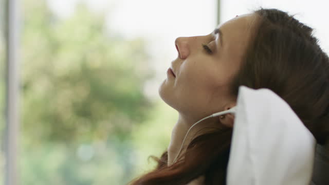 Pregnancy woman lying down on day time bed relaxing enjoying music