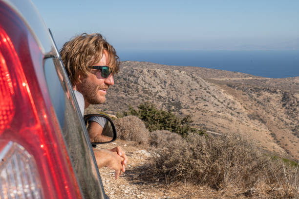 istock Young man inside a car looks at view, road trip concept 1358597333
