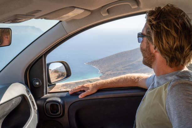 istock Young man inside a car looks at view, road trip concept 1358597945