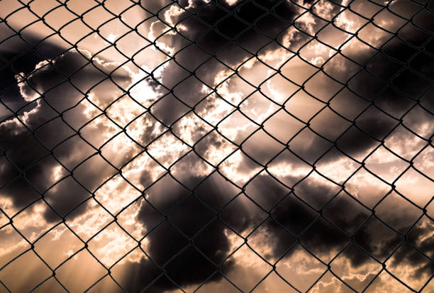 old steel mesh chain-link against the backdrop of an alarming stormy sky. The concept of the social problem of violation of human rights and personal freedom