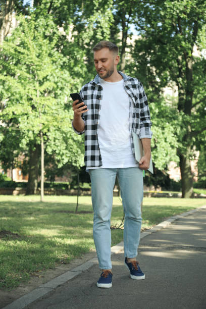 istock Young man with smartphone in park on summer day 1358601472
