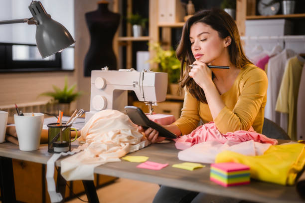 jovem empreendedora trabalhando em sua pequena oficina, calculando despesas, fazendo plano de negócios - tax tax form finance small business - fotografias e filmes do acervo