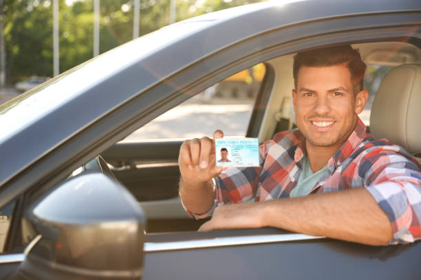 istock Happy man holding license while sitting in car outdoors. Driving school 1358602638