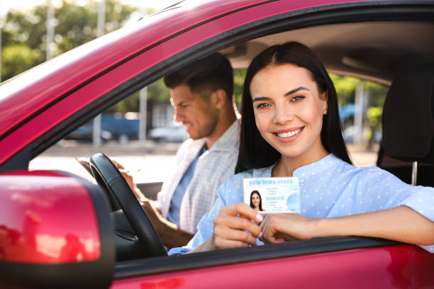 istock Young woman holding license while sitting in car with instructor. Driving school 1358602961