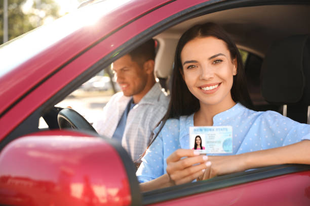 istock Young woman holding license while sitting in car with instructor. Driving school 1358602962
