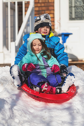 Brother & sister enjoy sledding in their front yard after a snowstorm.