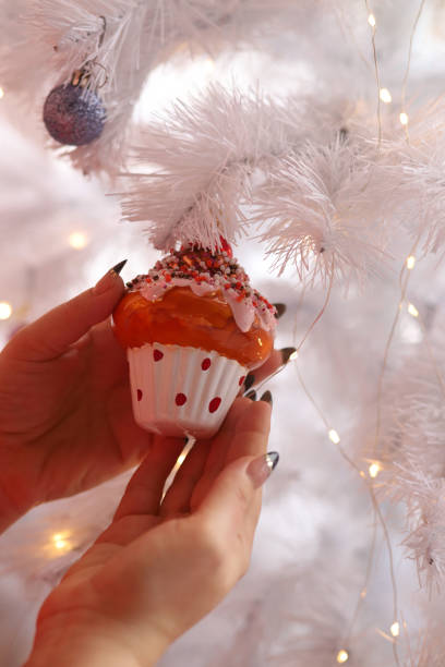 istock woman's hand hangs a toy on an artificial Christmas tree. Vertical orientation 1358615328