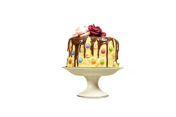 Birthday layer cake decorated with chocolate pieces and happy birthday text, hazelnuts and roses flowers isolated on white