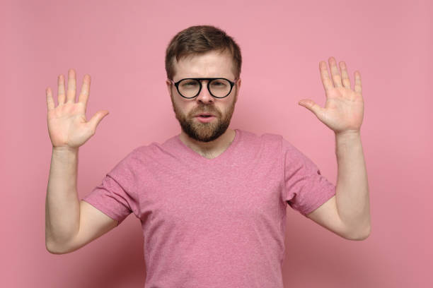 istock Confident man in glasses makes a stop gesture, he raises hands up and shows palms, looking with a squint at the camera. 1358619976