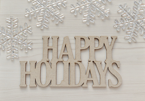 Closeup of a Happy Holidays message on a whitewashed wood background with snowflake ornaments.