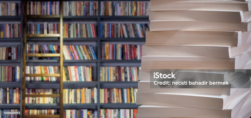 stacks of papers book pages stacked in front of blurred library background Book Stock Photo