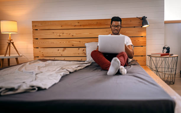 istock Man sitting on bed working on laptop 1358627029