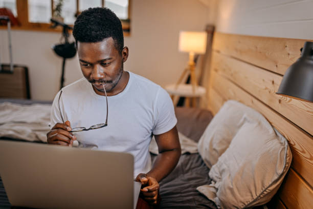 istock Man sitting on bed working on laptop 1358627153