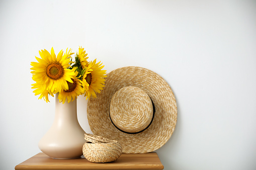 Bouquet of beautiful sunflowers, wicker basket and hat on table indoors