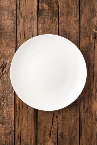 Overhead shot of blank white dish on rustic wooden table. Close up