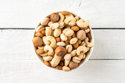 Mixed dried nuts (almonds, pistachios, peanuts, hazelnuts and cashews) in bowl on wooden table. Top view