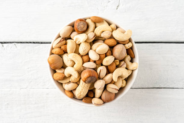 Mixed dried nuts (almonds, pistachios, peanuts, hazelnuts and cashews) in bowl on wooden table. Top view stock photo