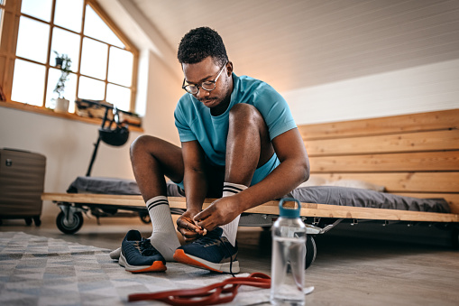 Young fit and healthy men wearing shoes while getting ready and preparing for home workout in the morning