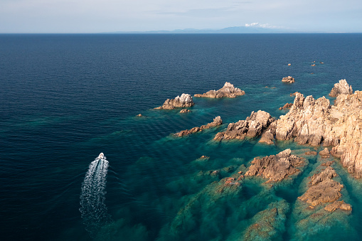 Aerial tracking shot of a motorboat in motion, on an amazing blue sea near the rocky rough coast.