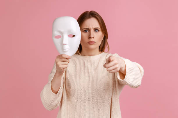 mulher estrita apontando o dedo para a câmera, segurando máscara branca na mão, quer mudar de personalidade. - mask hiding women dishonesty - fotografias e filmes do acervo