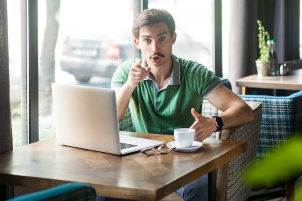 istock Man working on laptop, pointing finger, indicating direction to camera, looks annoyed, making choice 1358639088