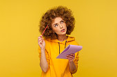 Pensive woman with Afro hairstyle holds notepad and pencil in hands thinking over plans for startup.